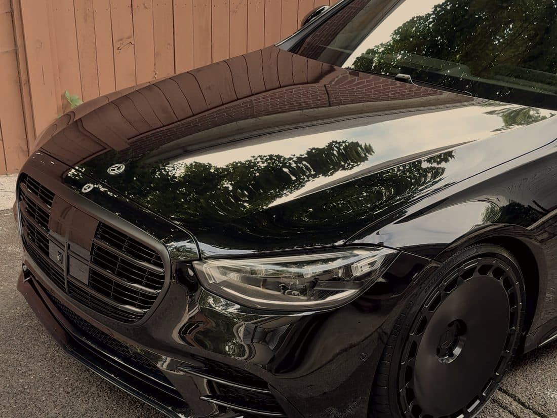 Black Mercedes S-Class with the fence behind it reflected in the paint