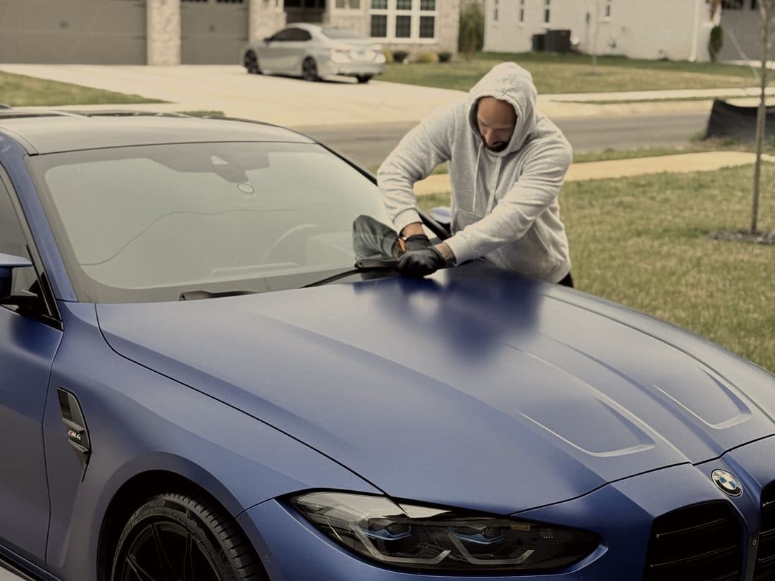 Detailer wiping down the hood of a frozen blue BMW M4