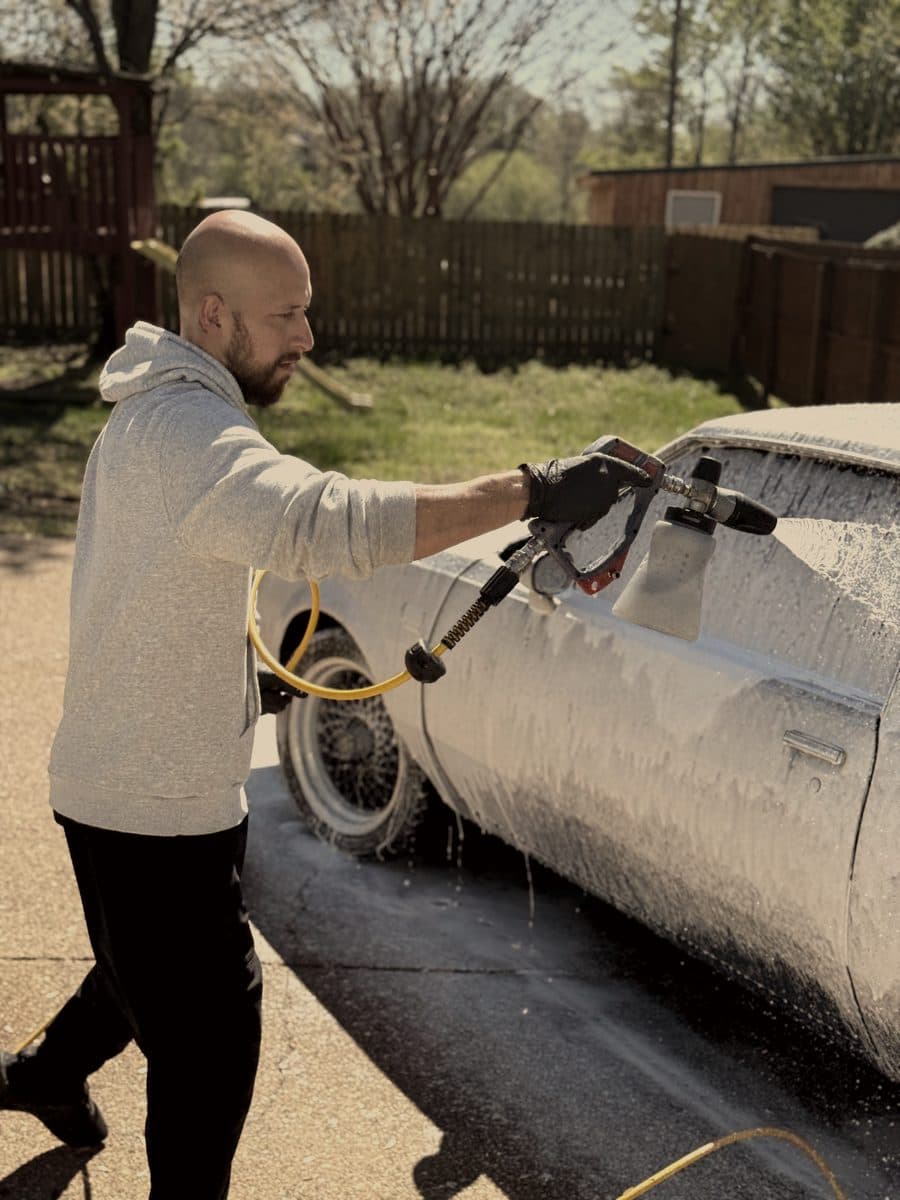 Detailer spraying foam over a car with a pressure washer
