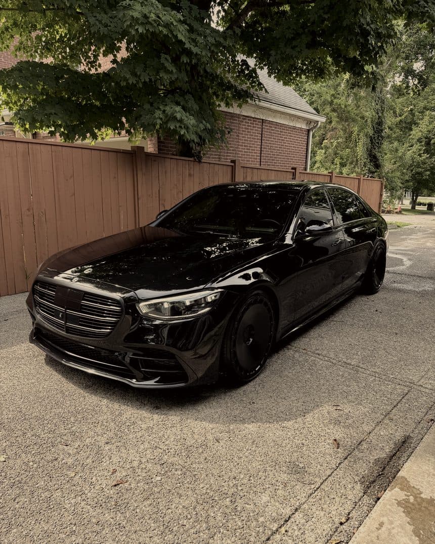 Black Mercedes S580 in profile beside a wooden fence
