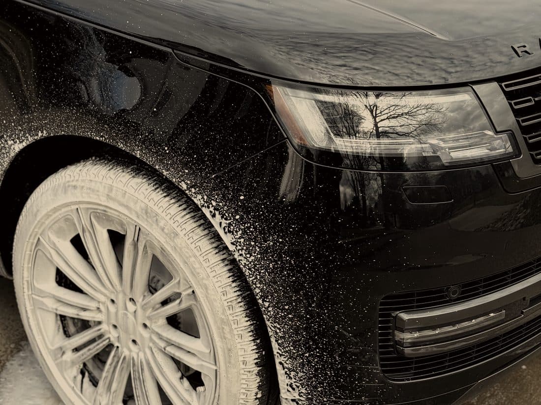 Foam running off the wheel of a black Range Rover during the pre-wash