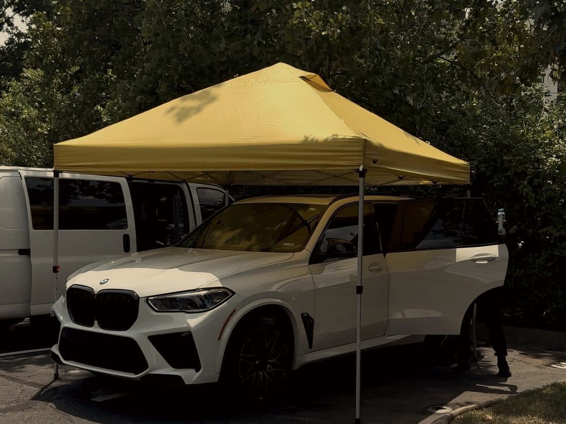 White BMW X5 M under the mobile canopy beside the work van