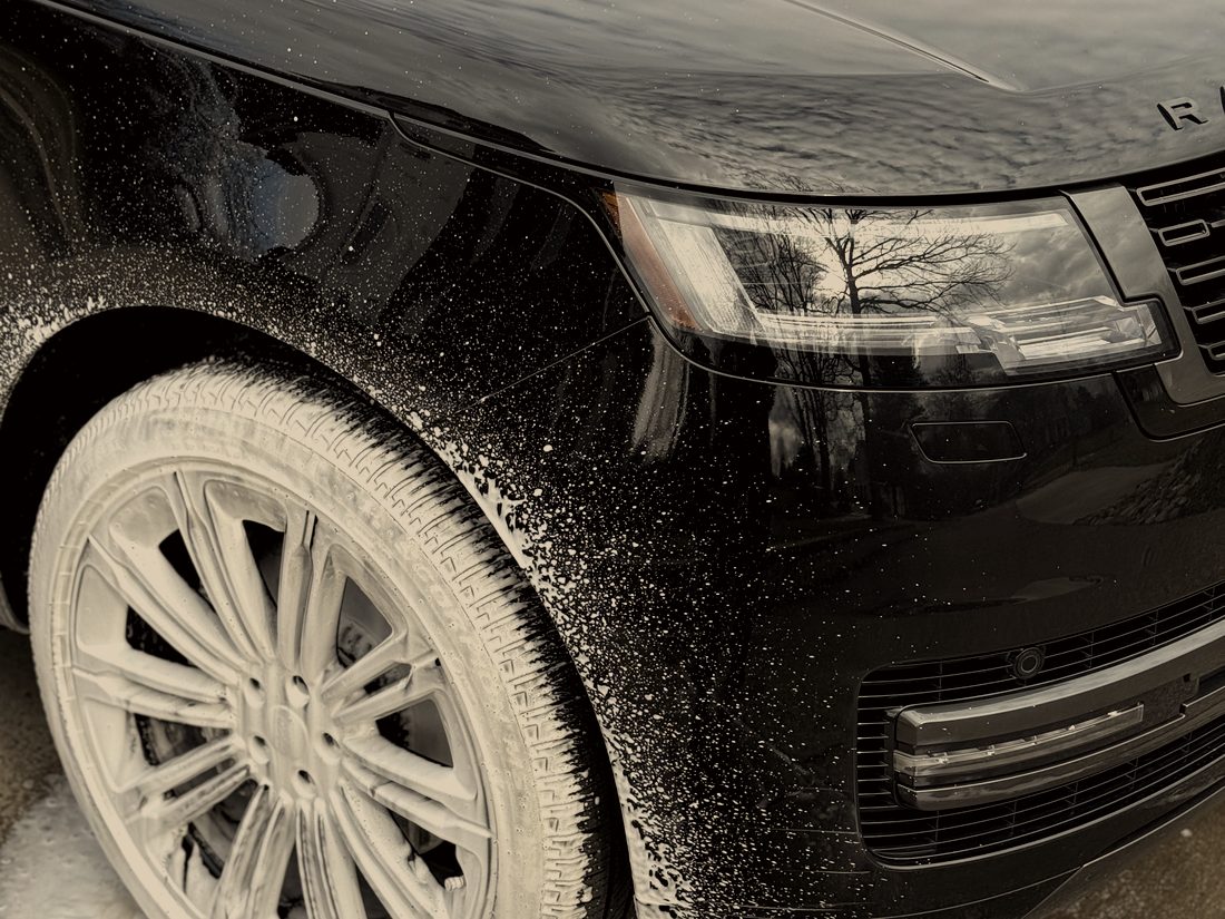Foam running off the wheel of a black Range Rover during the pre-wash